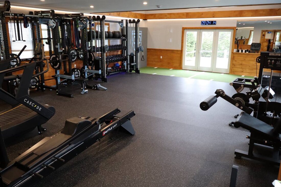 Strength and conditioning floor with racks, dumbbells, sleds, and a turf strip leading to French doors