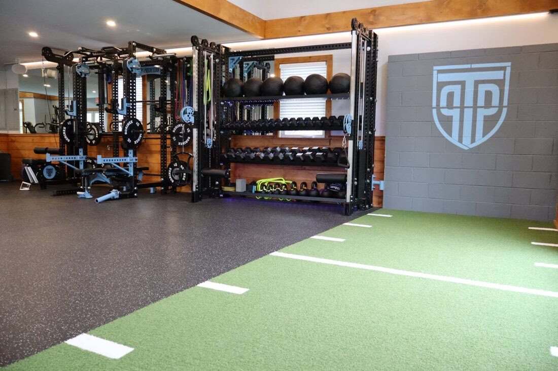 PT Progression's turf strip and strength racks, with the shield logo on the wall